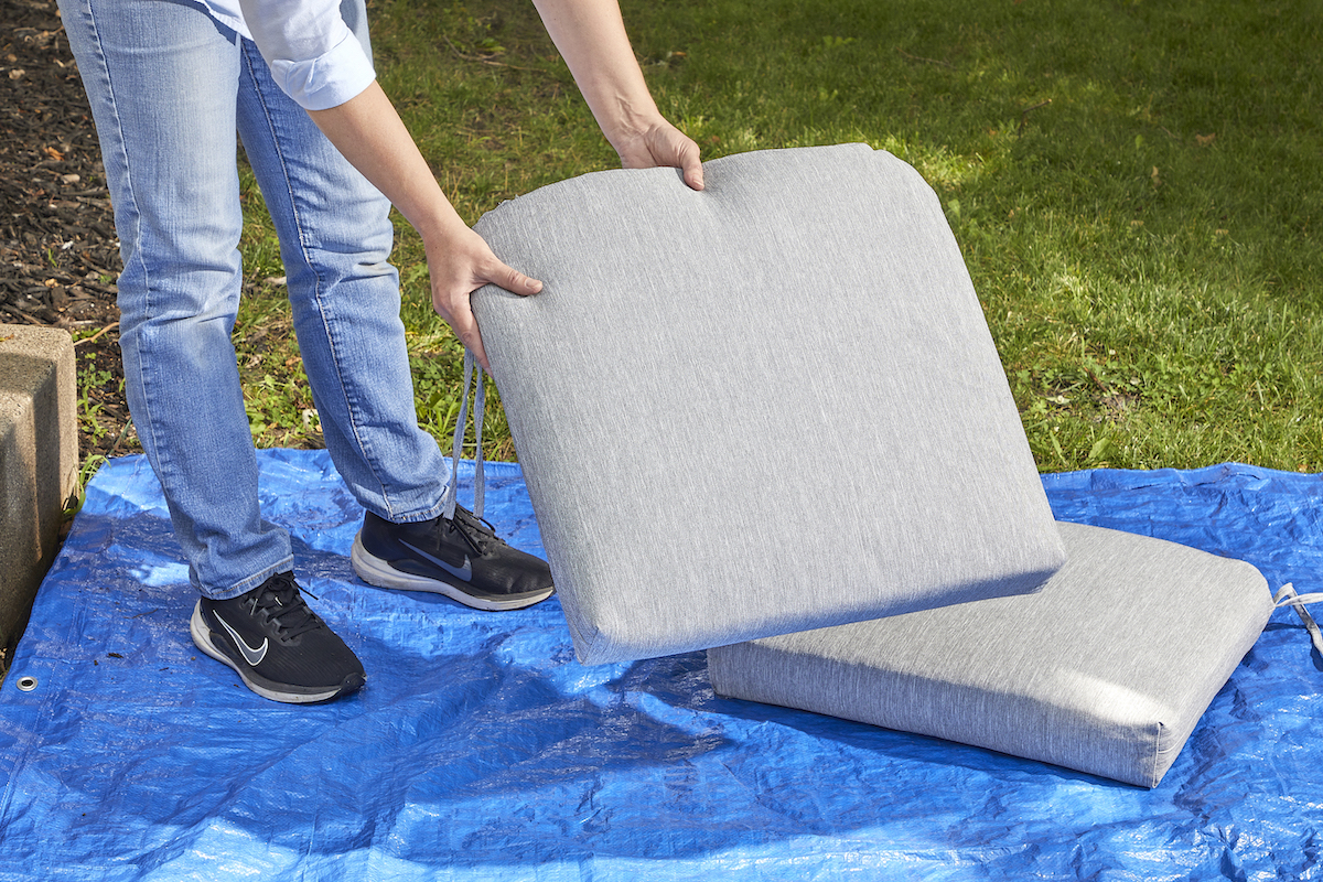 Woman lays two grey patio cushions on a blue tarp.