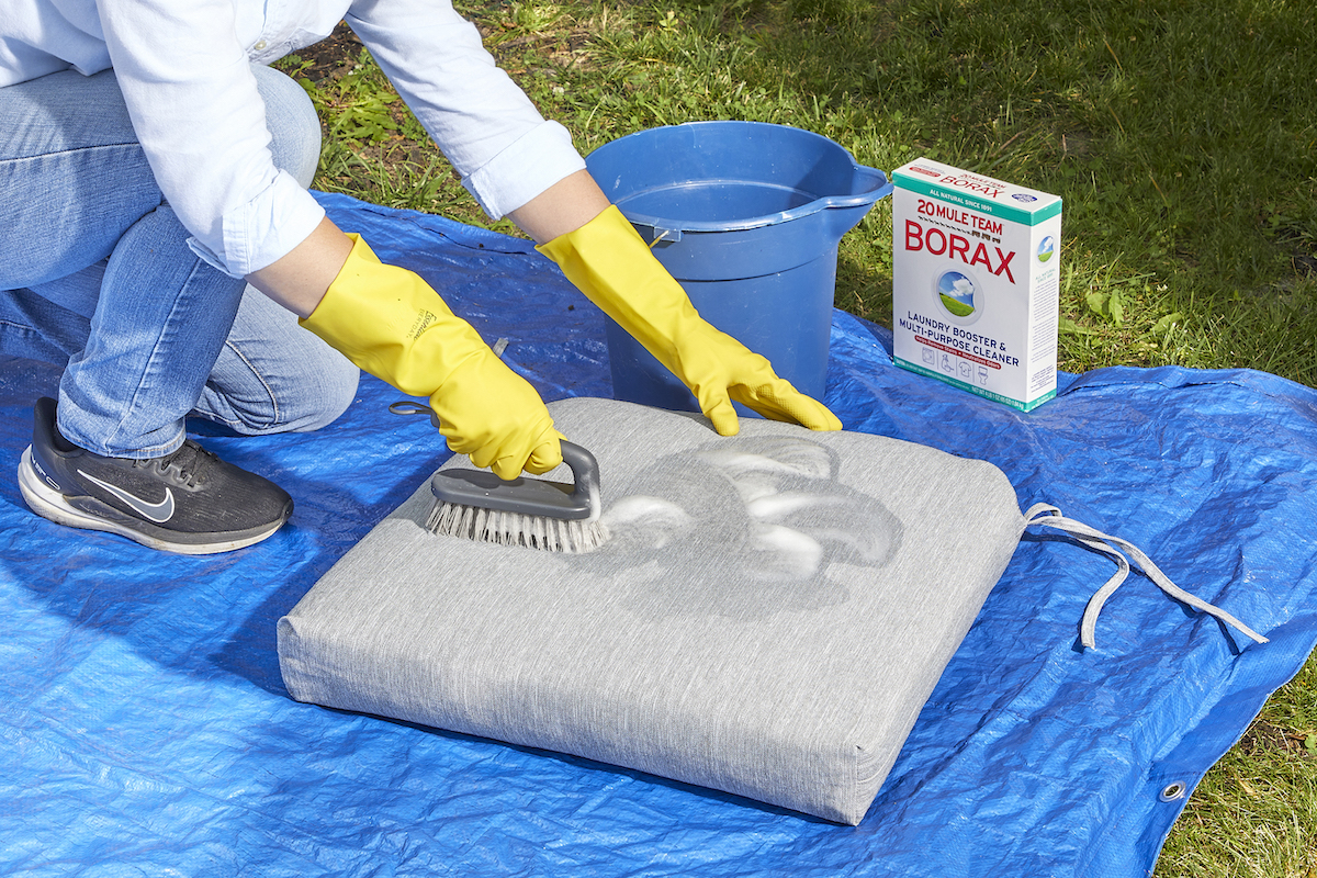 Woman uses cleaning solution to remove mold and mildew from patio cushions.