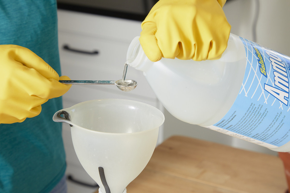 Woman measures ammonia into a measuring spoon poised over a funnel.