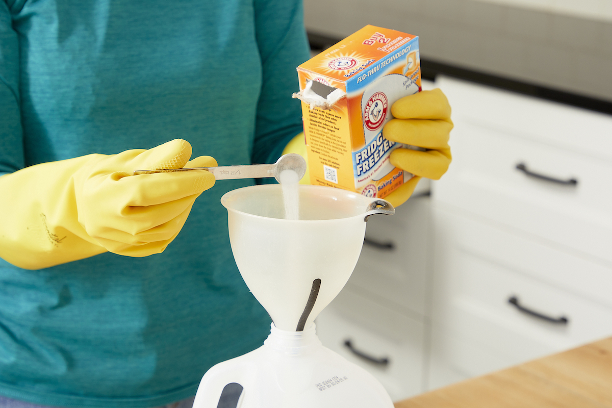 Woman measures baking soda into a funnel atop a 1-gallon jug.