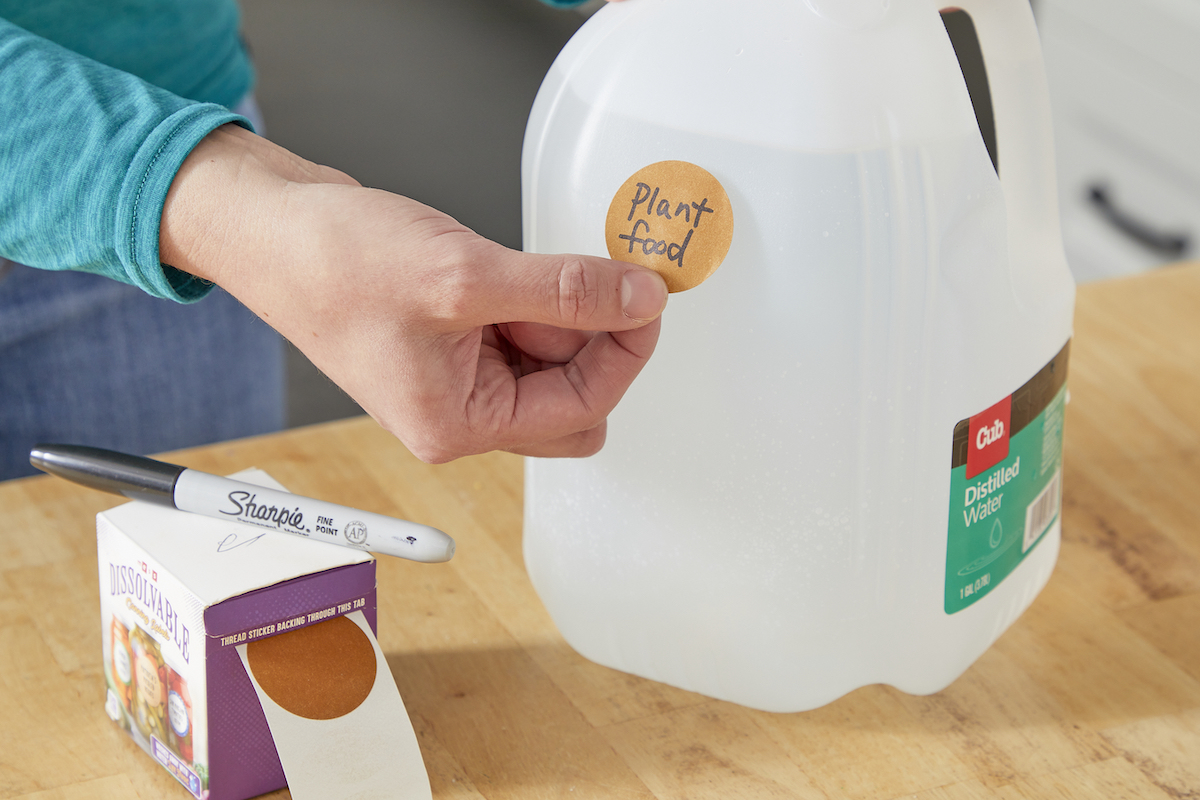 Woman labels a gallon jug with a round sticker that says "plant food."