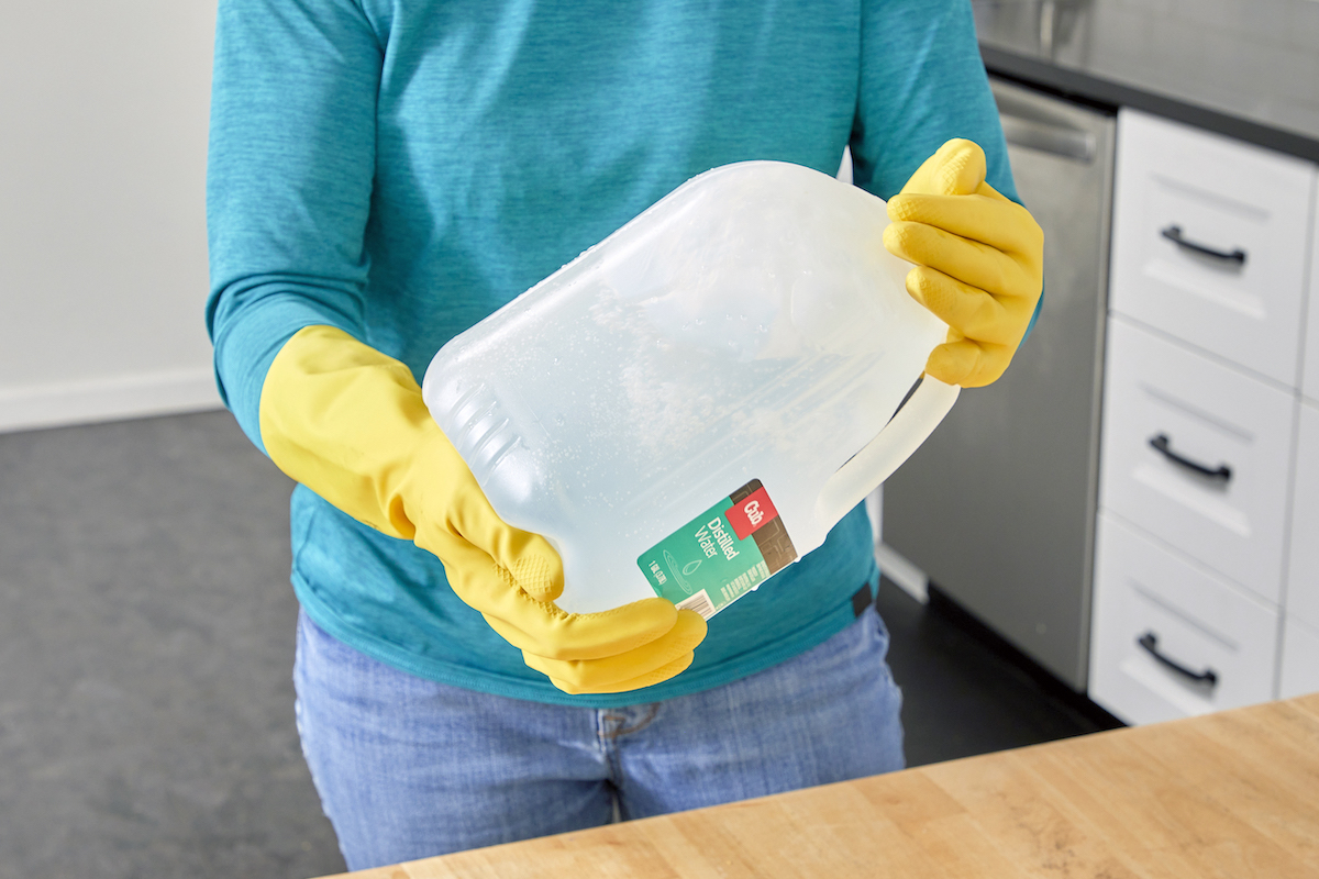 Woman wearing rubber gloves shakes a gallon jug of water.