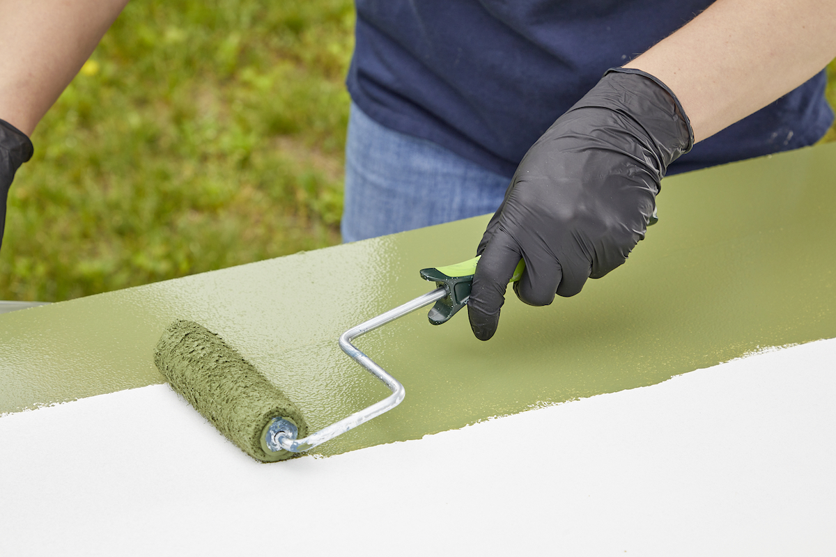 Woman uses small paint roller to apply green paint to a sheet of primed MDF.