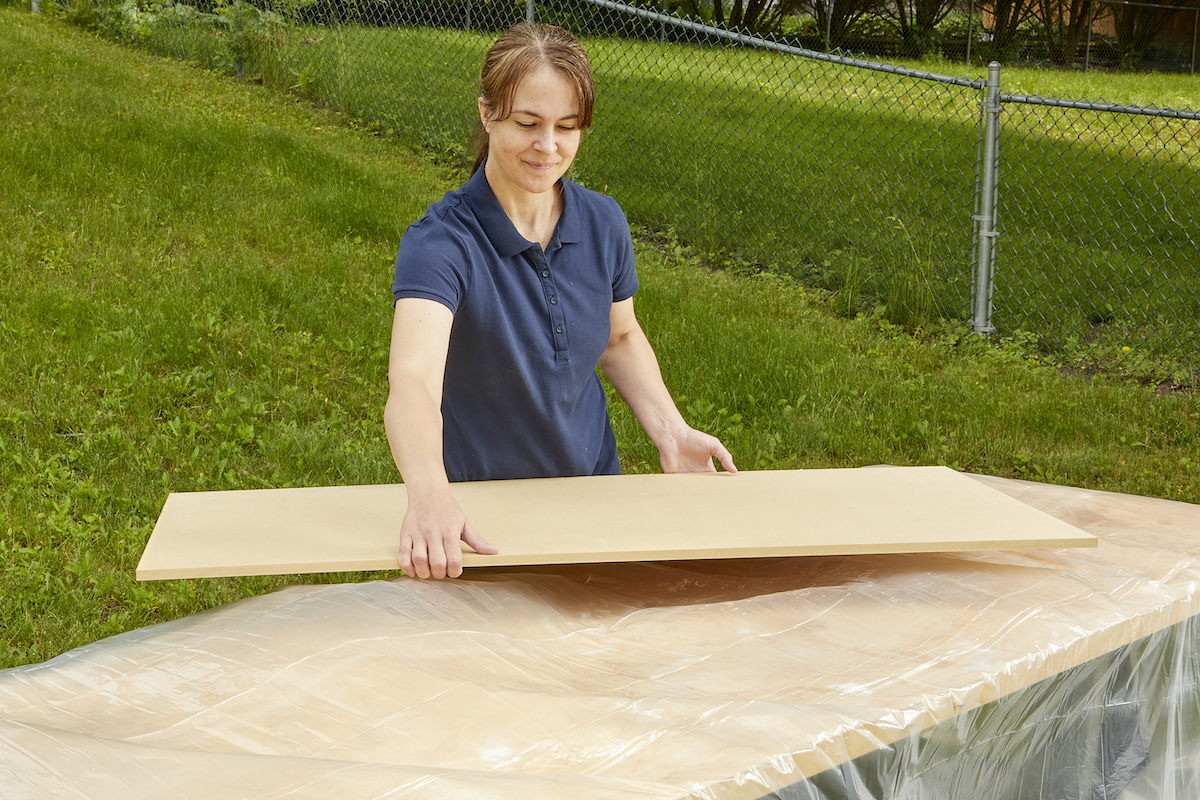 Woman prepares to lay a large piece of MDF onto a work table covered in plastic sheeting.