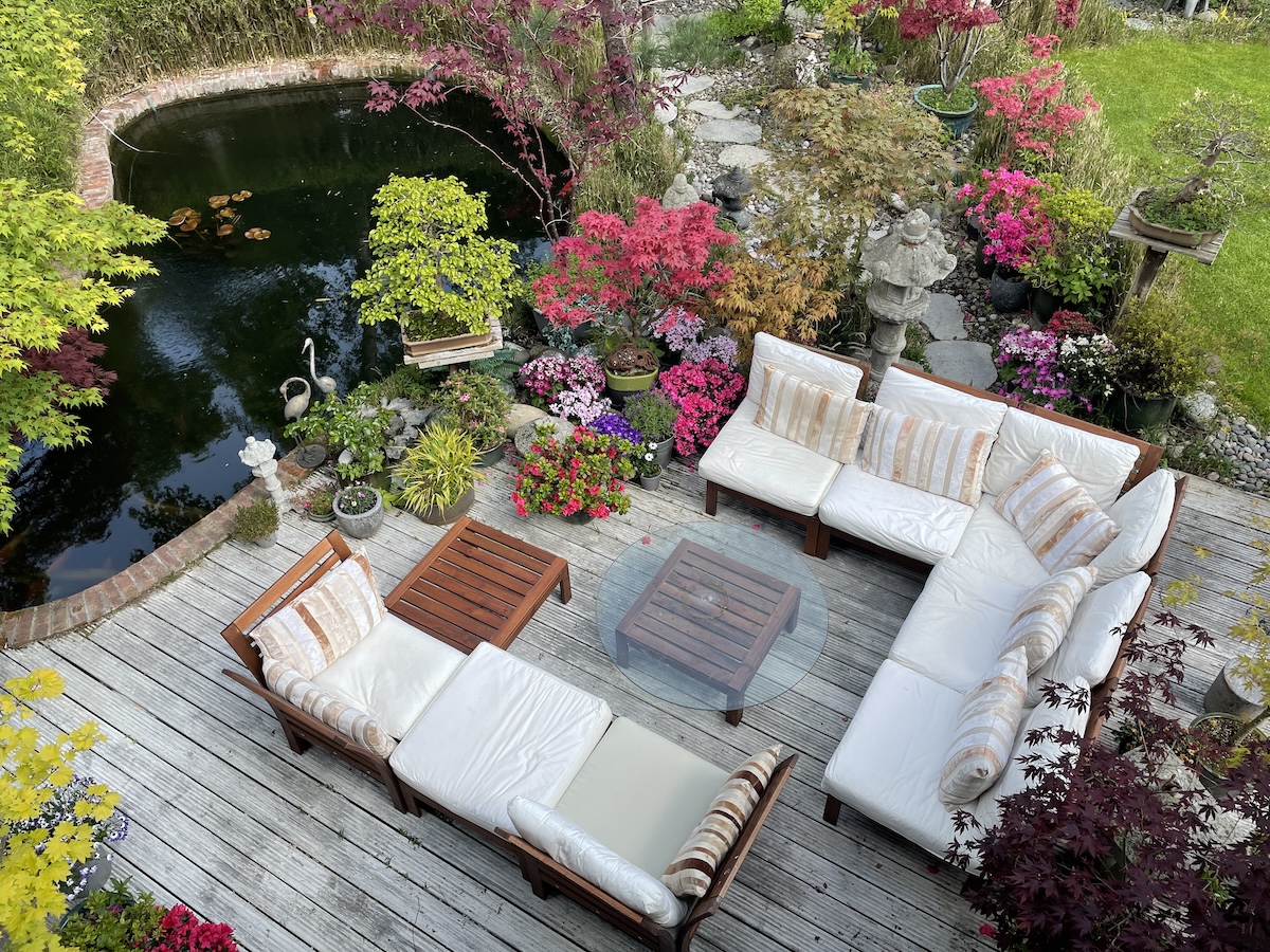 Outdoor patio with white furniture and colorful plants near a koi pond.