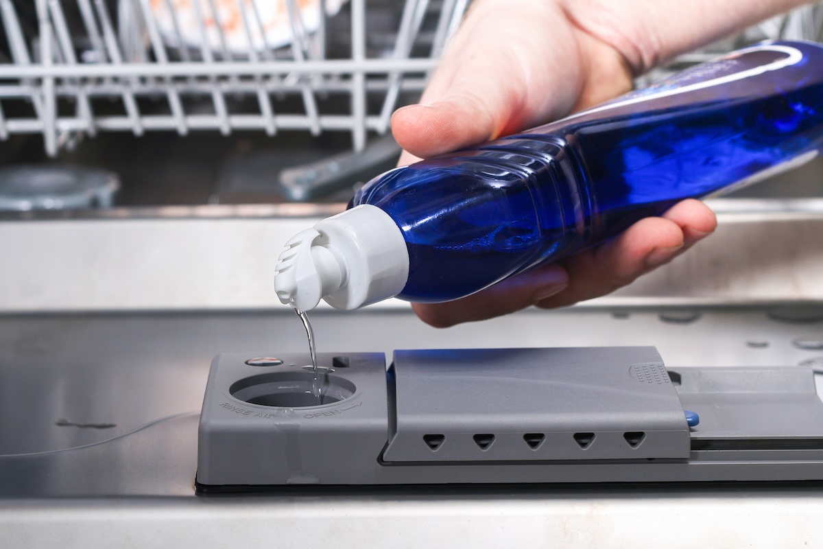 Pouring blue liquid into a dishwasher container.