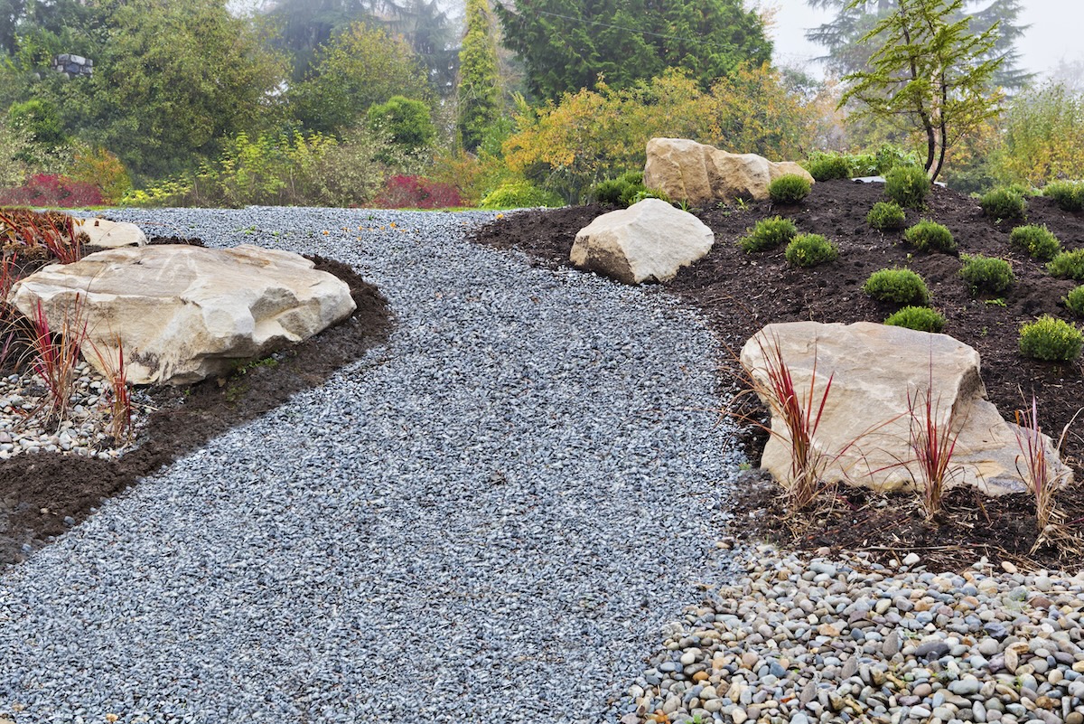 A gravel path between mulch landscaping and large stones. 