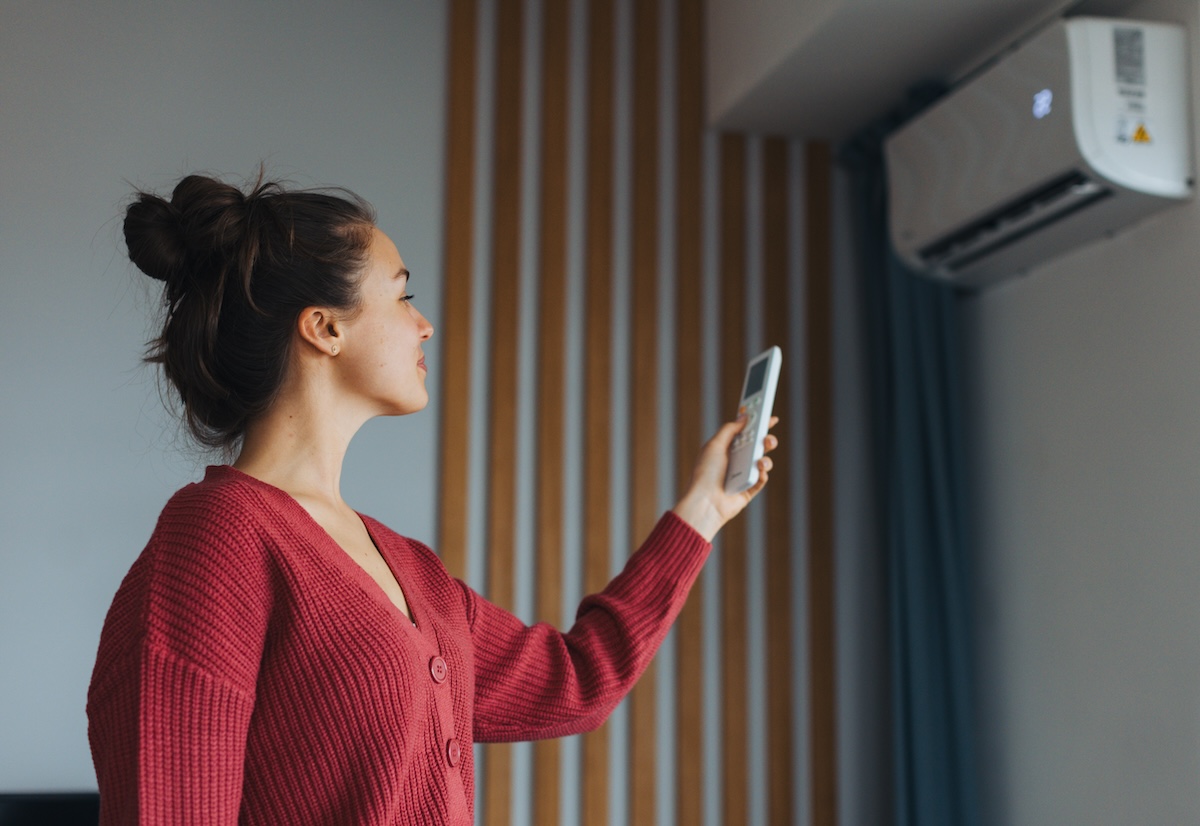 A young woman wearing a red sweater changes her home HVAC settings using a remote control.