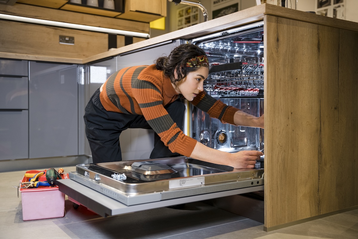 Young woman fixes bottom of dishwasher.