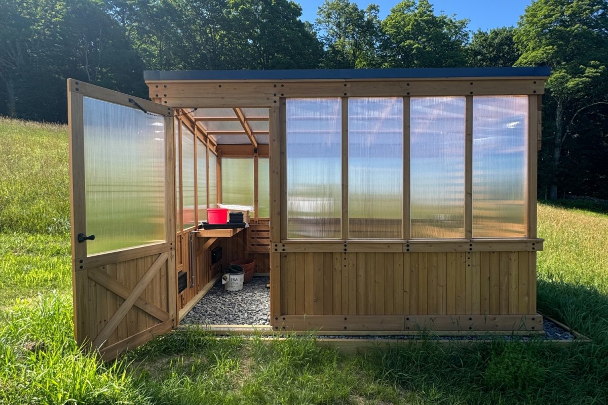 Cedar greenhouse on lawn with door open to reveal a red bucket inside