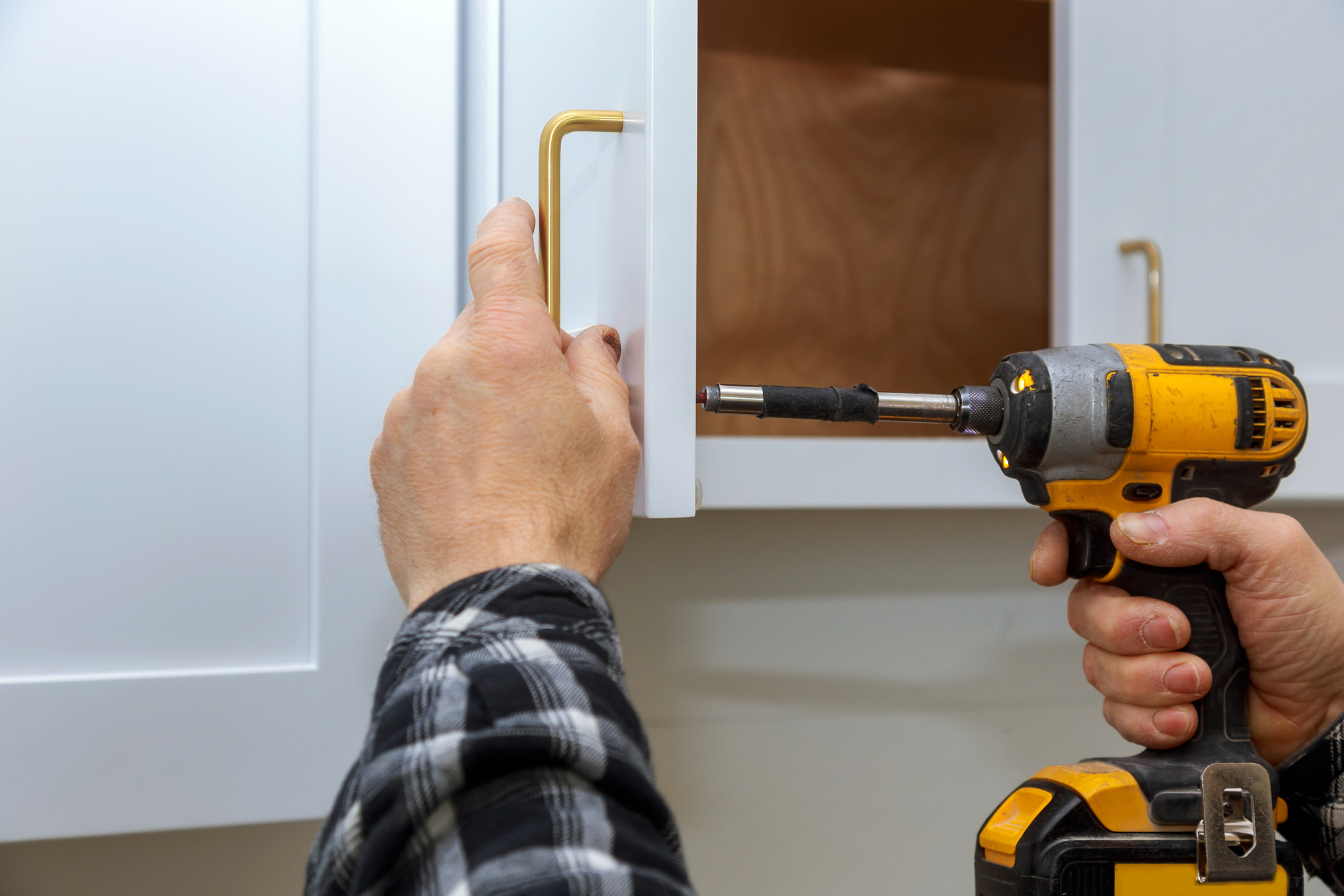 A person uses a power tool to install a new cabinet handle pull