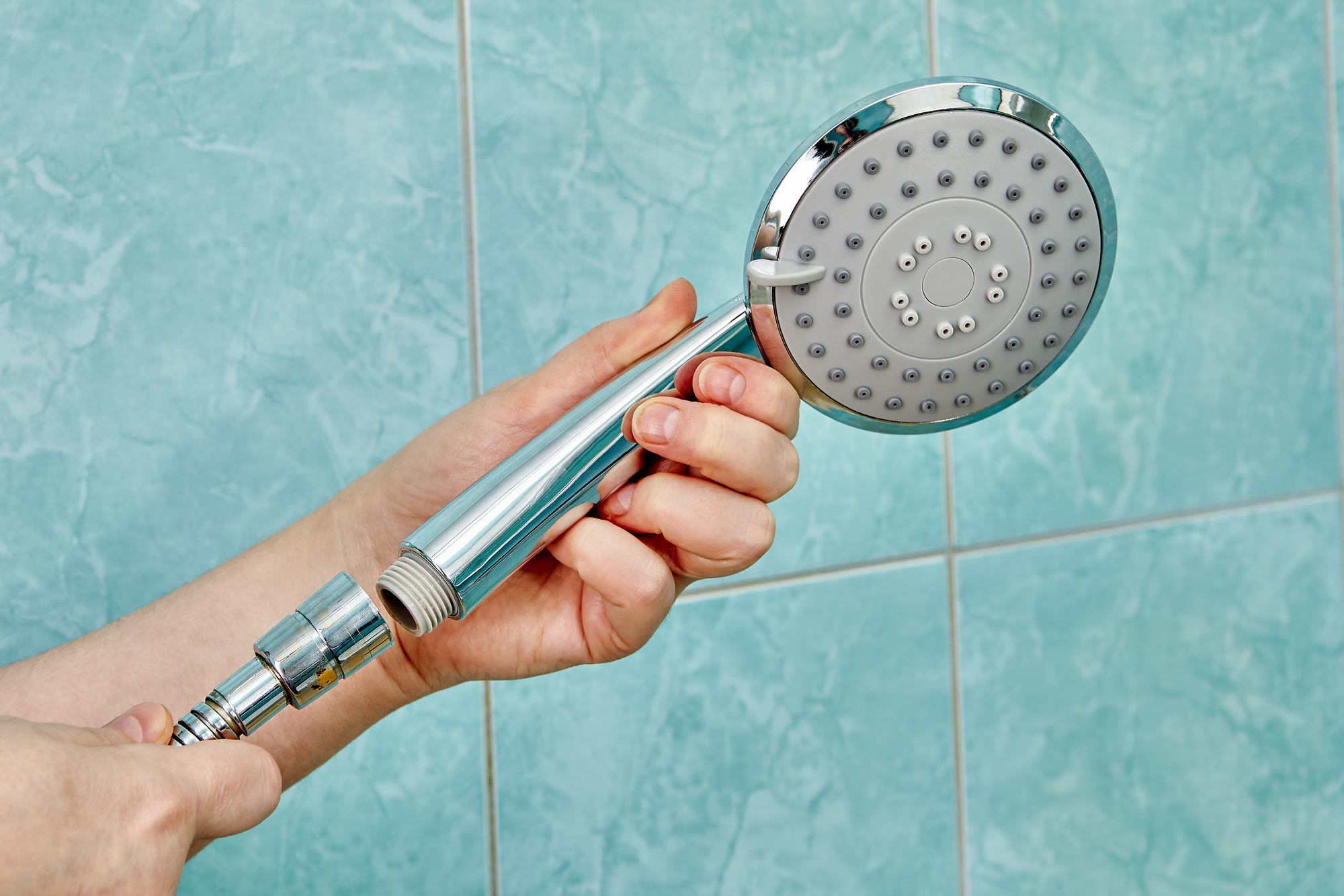 Hands are replacing old shower head by removing it from the flexible hose