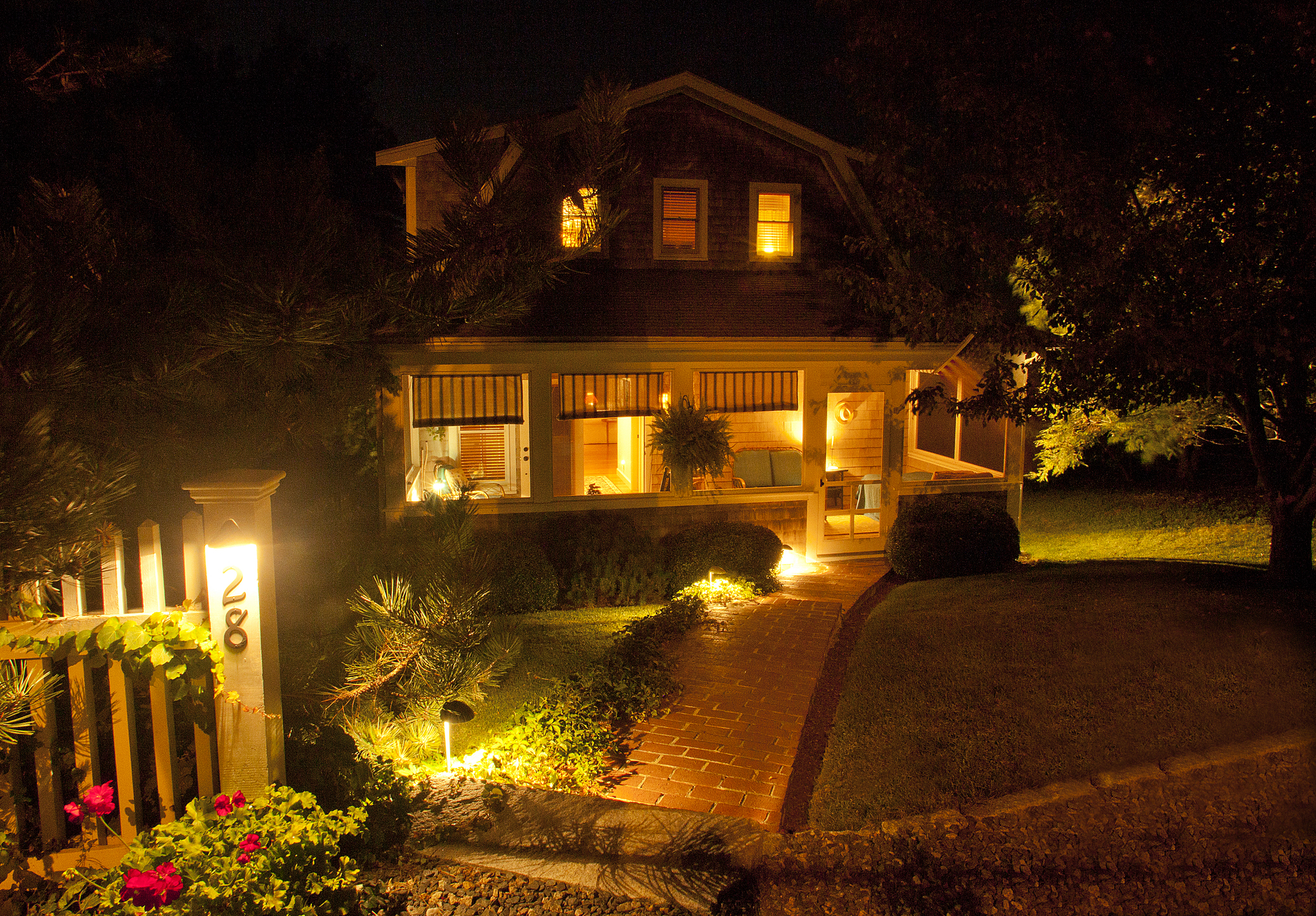 A cozy two story house with screened porch illuminated at night by path lights