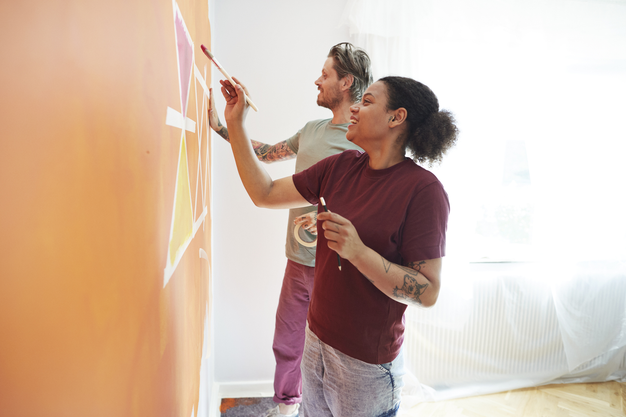 Couple painting an accent wall in the home in bright orange