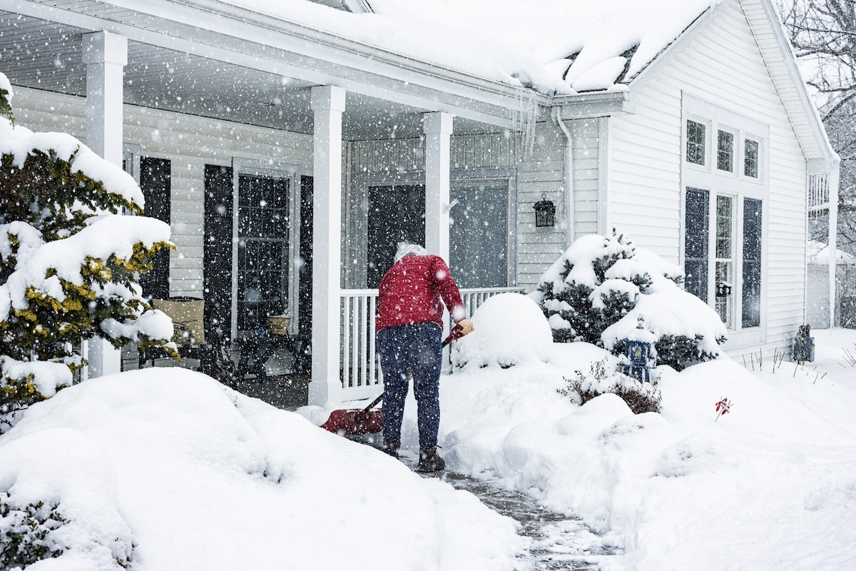 A homeowner shoveling snow away from the front door, porch, and walkway.