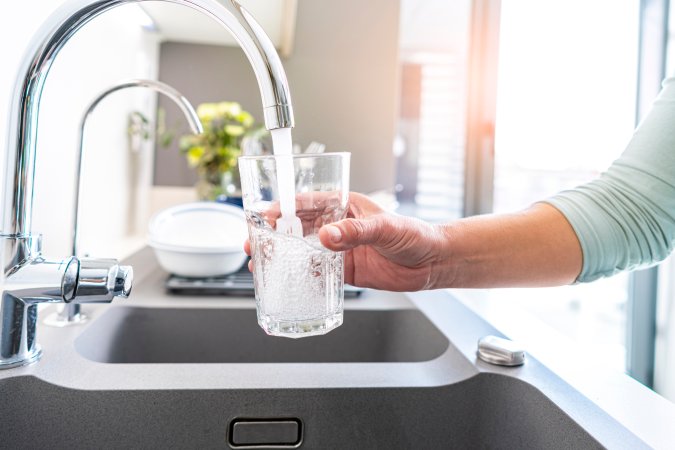 Close up of a woman hand filling a glass of water directly from the tap in the kitchen.