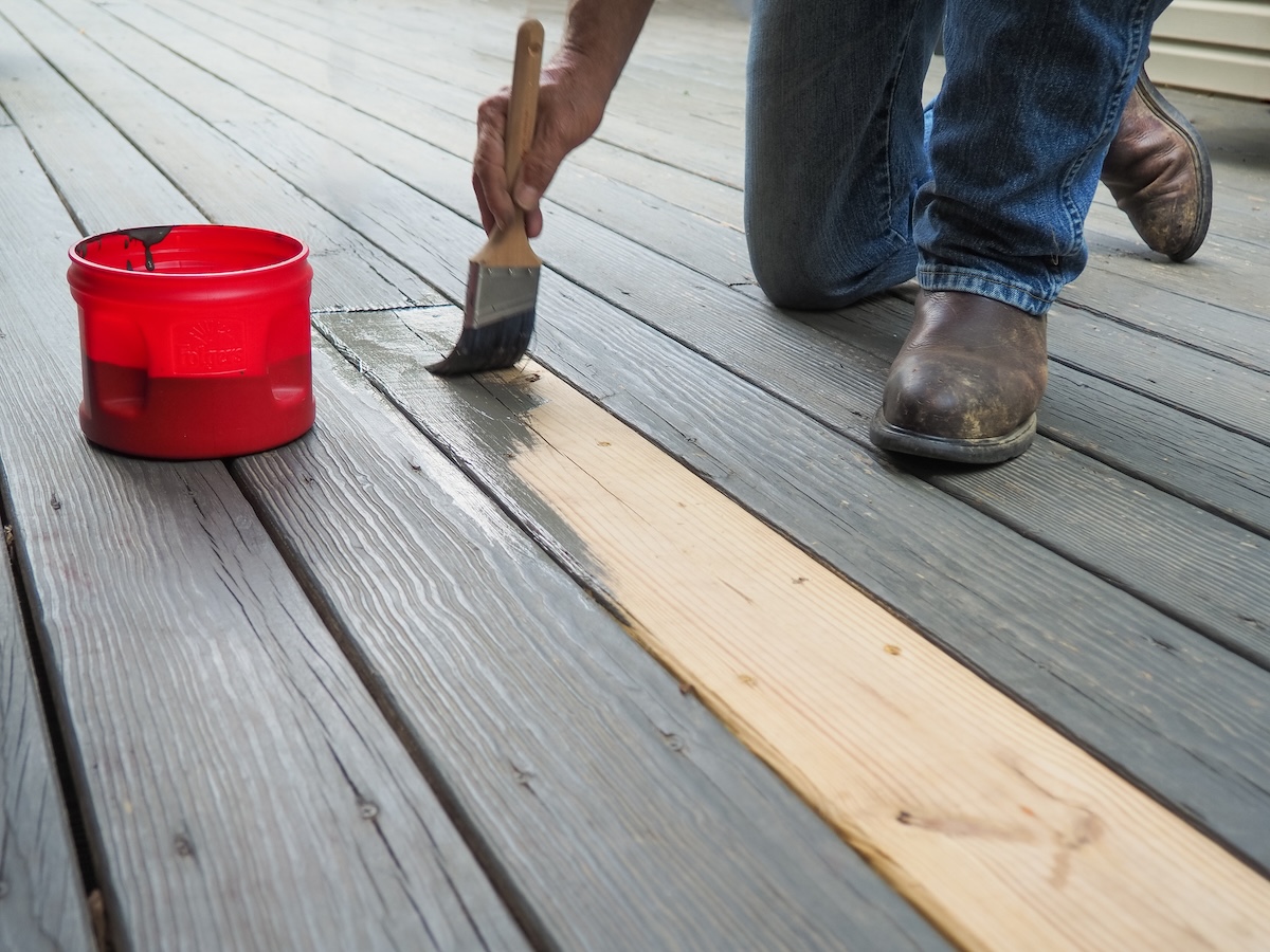 A person staining a new deck board to match the existing deck.