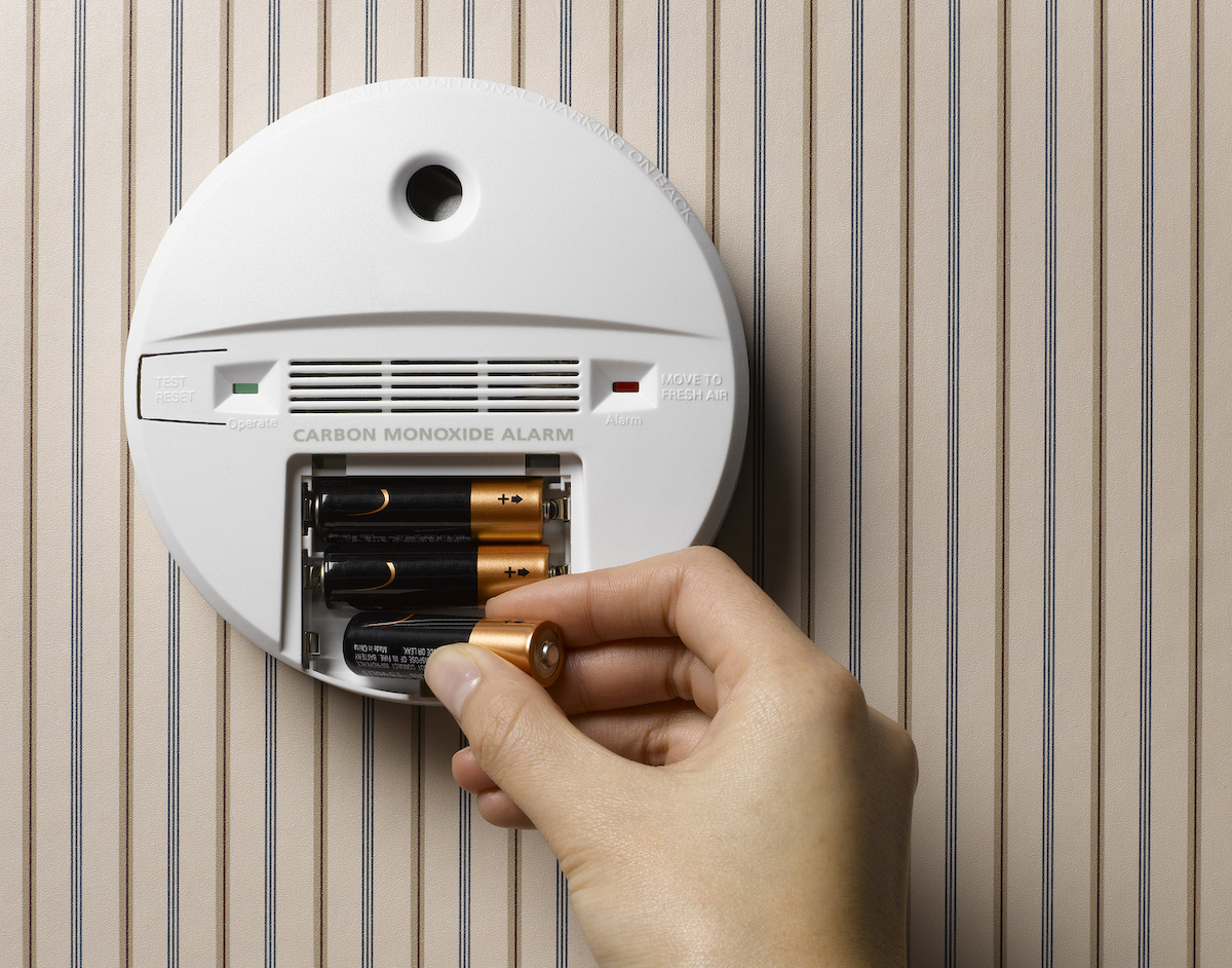 A person is replacing the batteries inside of a carbon monoxide detector.