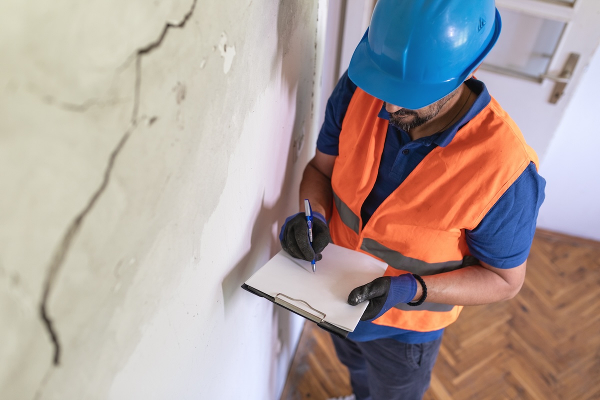 A foundation professional inspecting a large crack in a home foundation and walls.