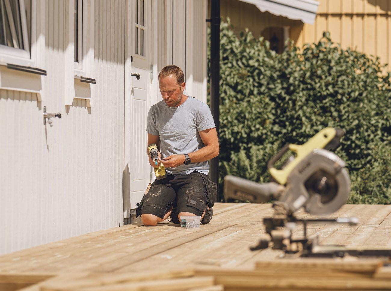 A person repairing a damaged deck board by replacing a single wood board.