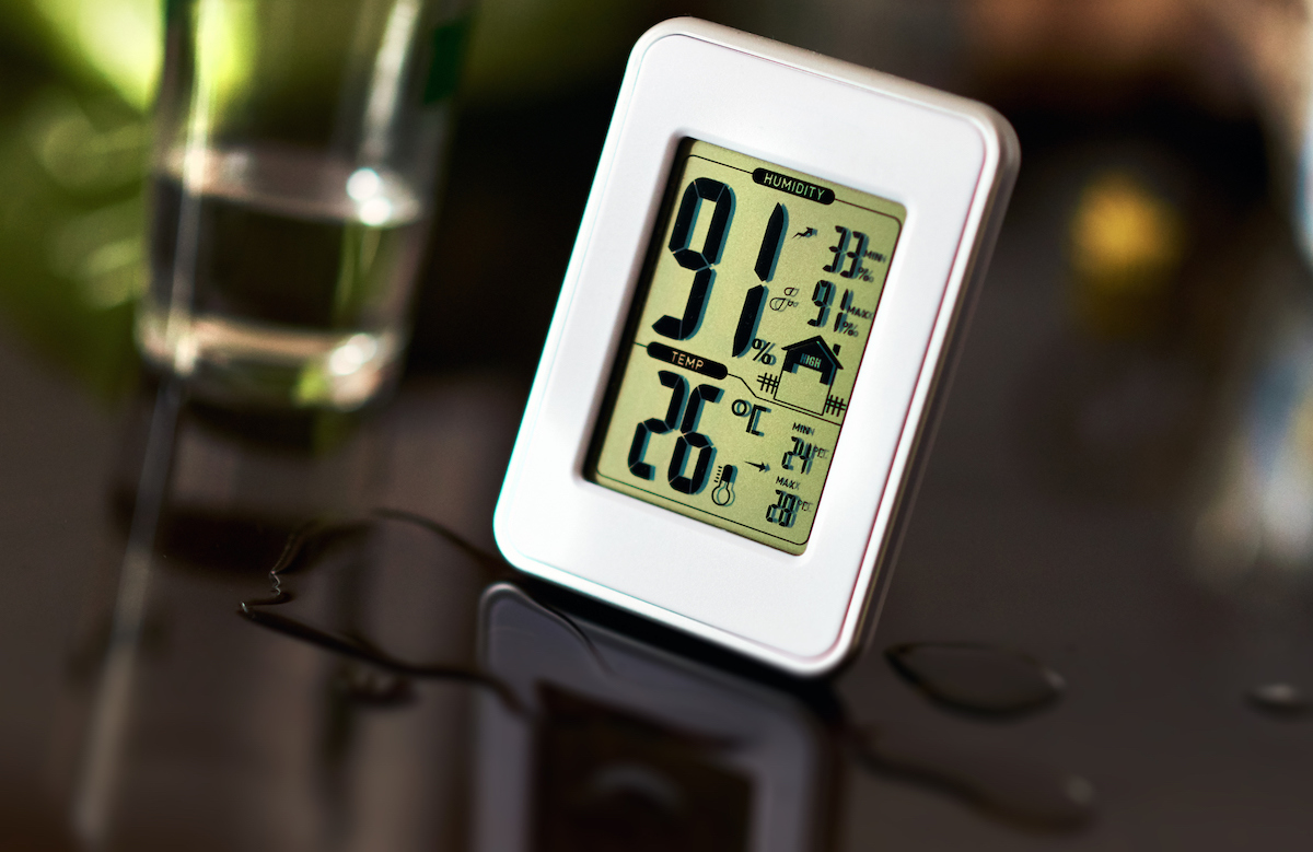 An electronic hygrometer and thermometer device is on top of a dark brown table with a small puddle in front of it.