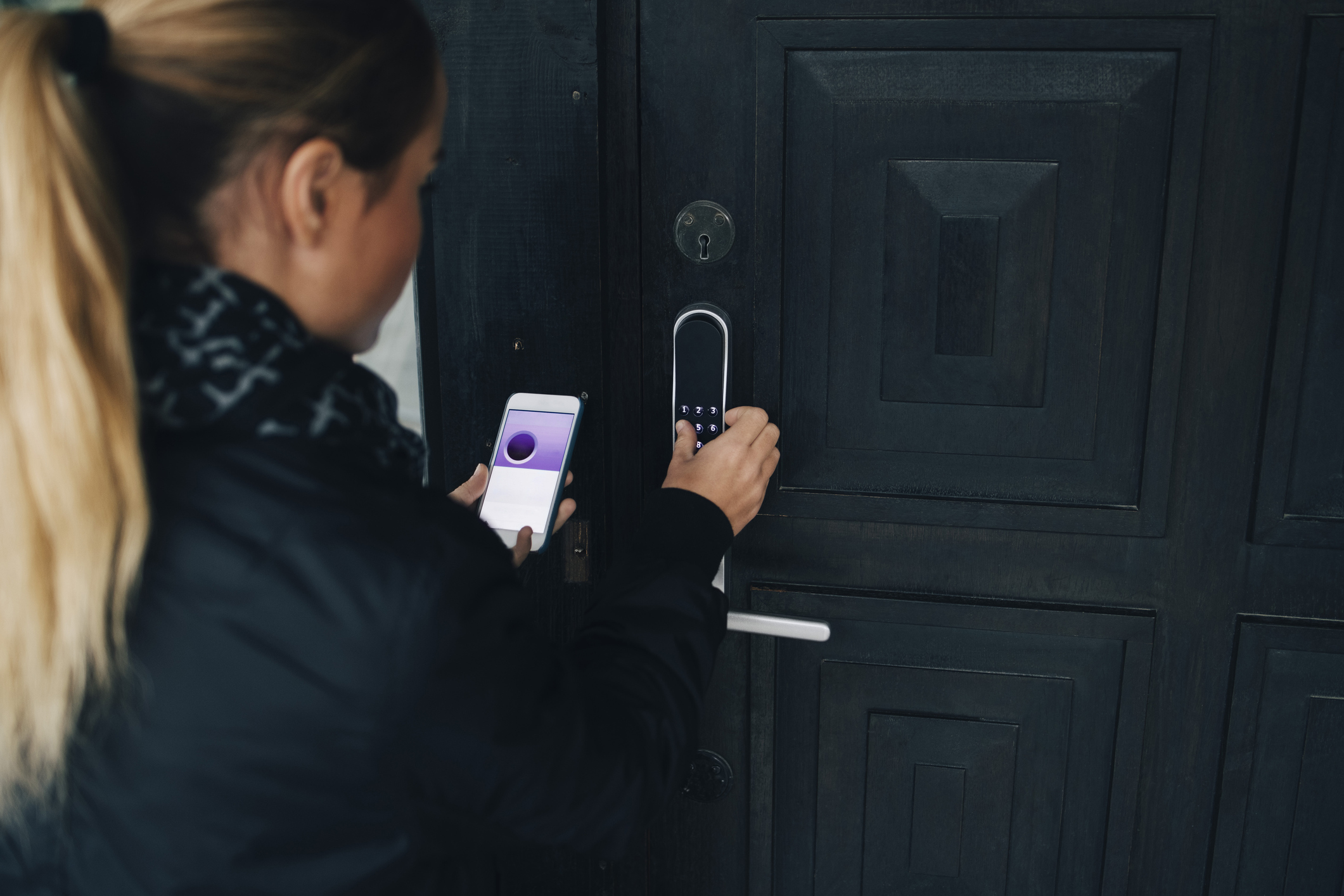 A person uses a smartphone and dials in the code to a smart lock on the front door