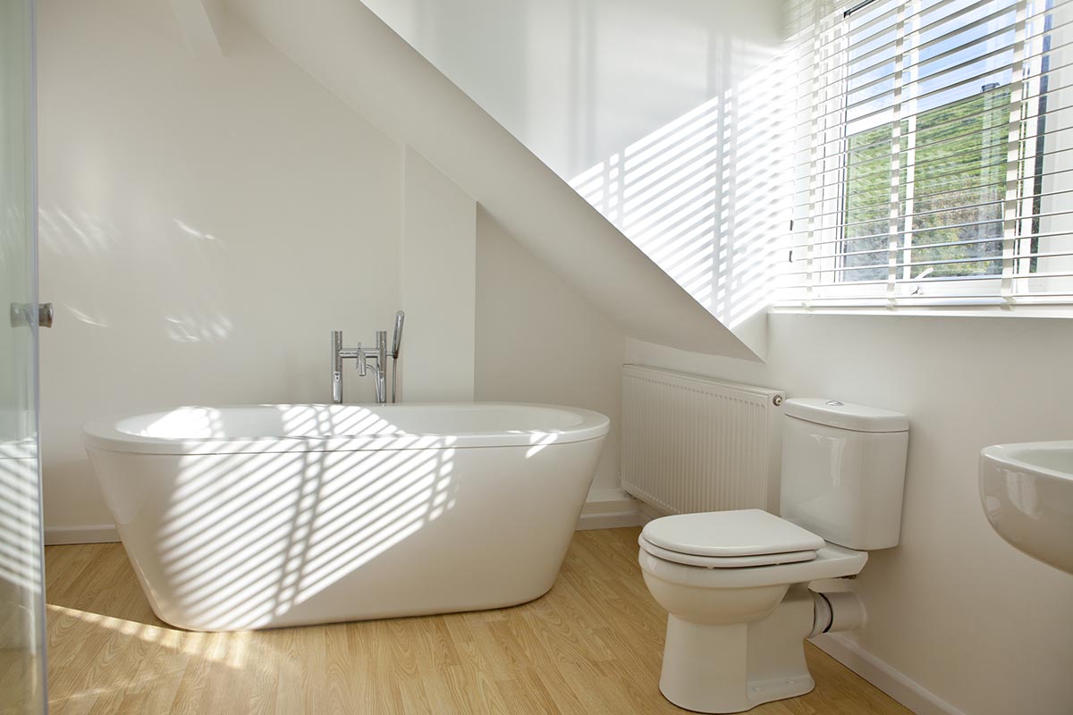 Light-colored wood flooring is installed in a bathroom with white walls and fixtures. 