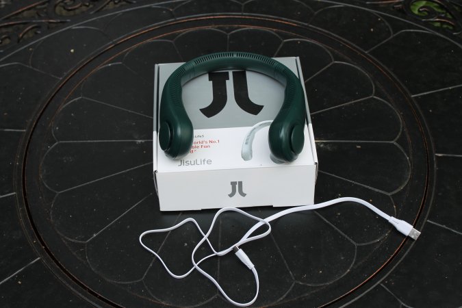 Green Jisulife Portable Neck Fan on top of its box with charging cord