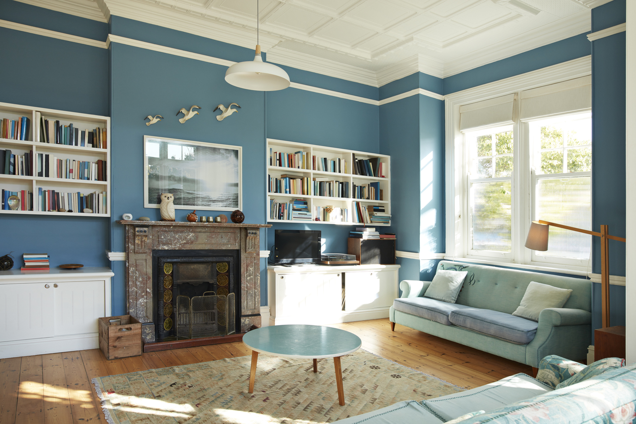 Two light-blue sofas are arranged to form a 90-degree angle in a living room with blue walls.