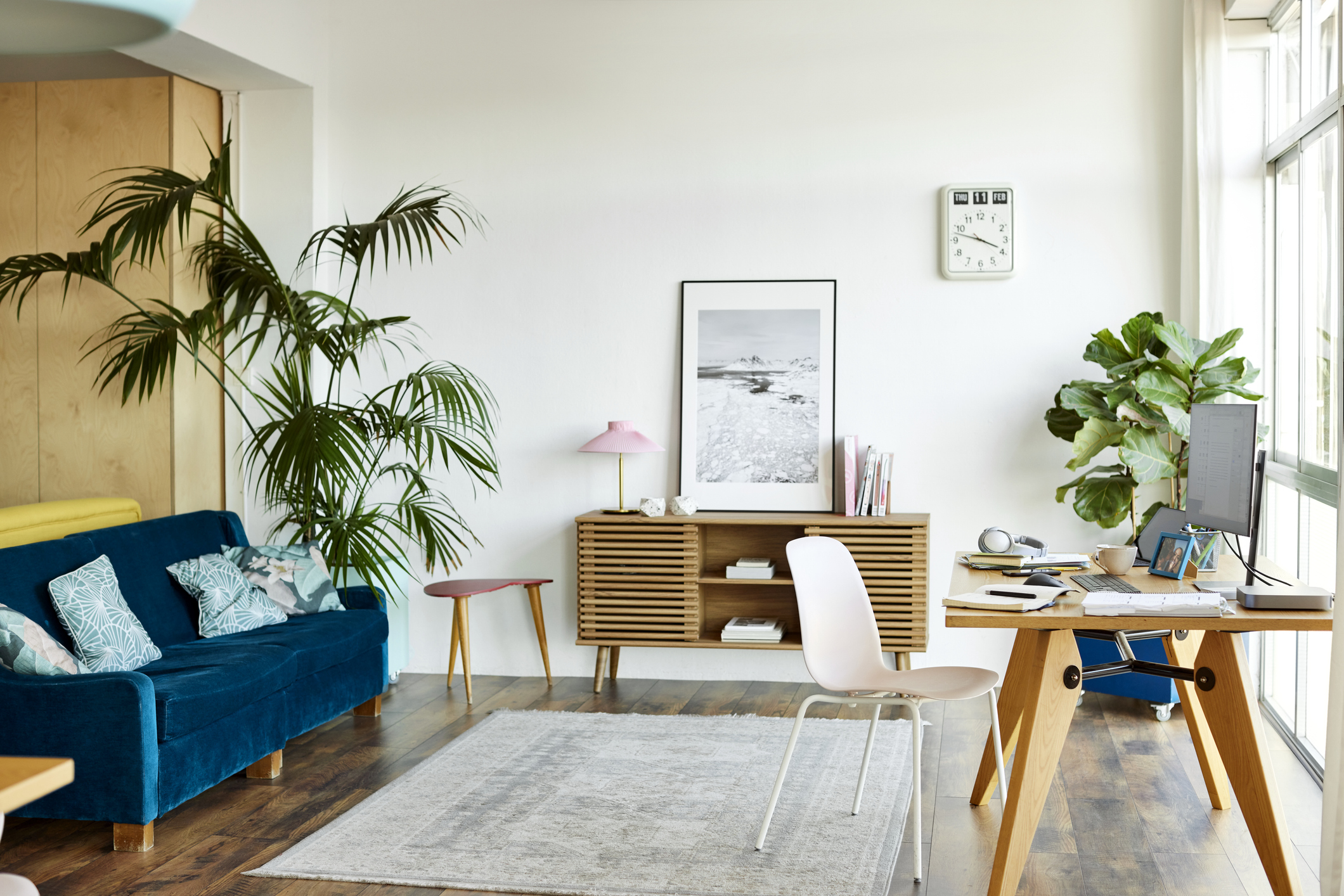 A colorful room furnished with a medium area rug, computer desk, blue velvet sofa, and a wood console table.