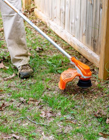 Person using Stihl FSA 80 R Battery Trimmer to cut grass along wood fence