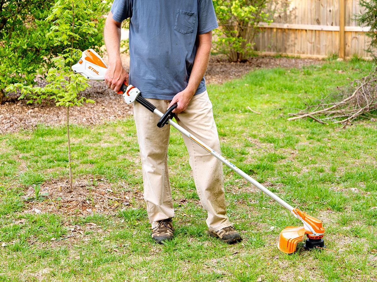 Person trimming tall weeds in the middle of a yard with a Stihl string trimmer