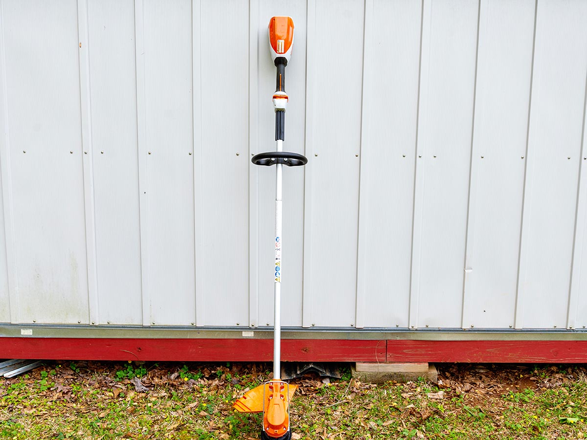 Stihl FSA 80 R Battery Trimmer leaning against a white shed on grass