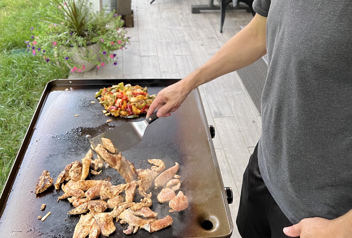 Person in gray shirt and black shorts cooking chicken fajitas on one of the best outdoor griddles