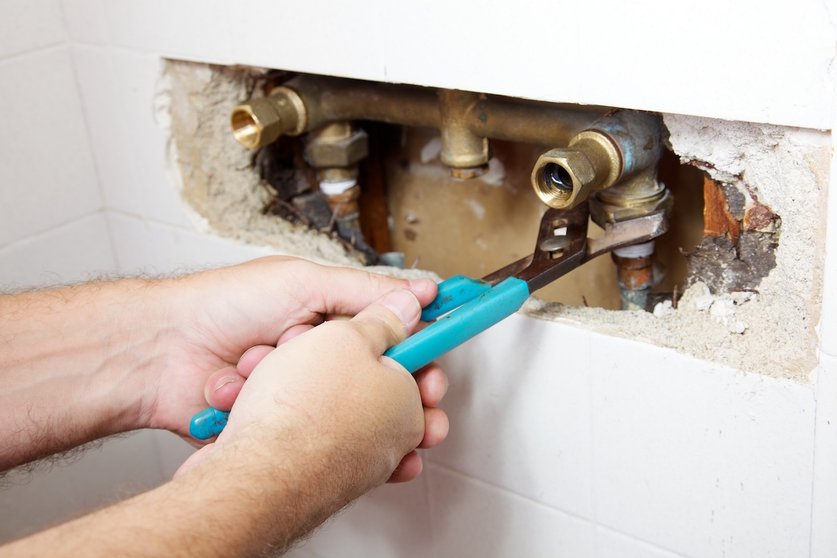 Using a wrench to fix a shower valve in a while-tiled shower.