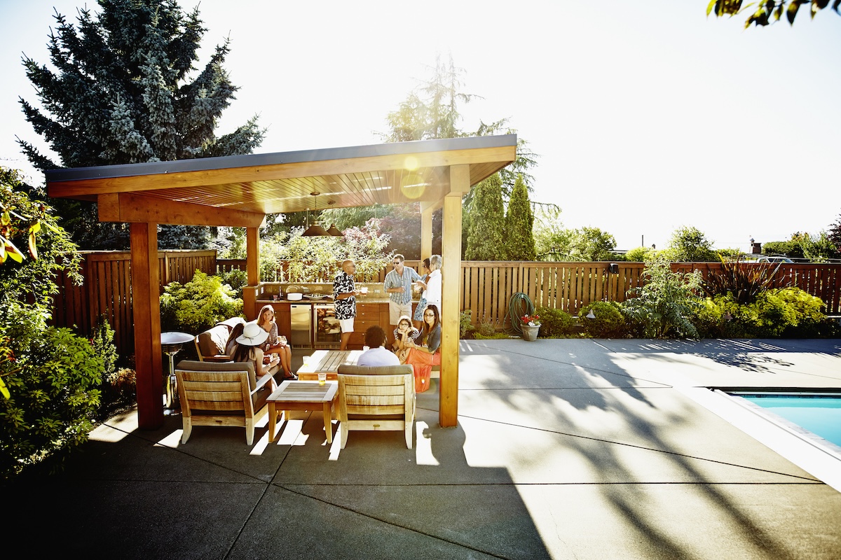 A group of friends eating under a wooden cabana in a backyard.