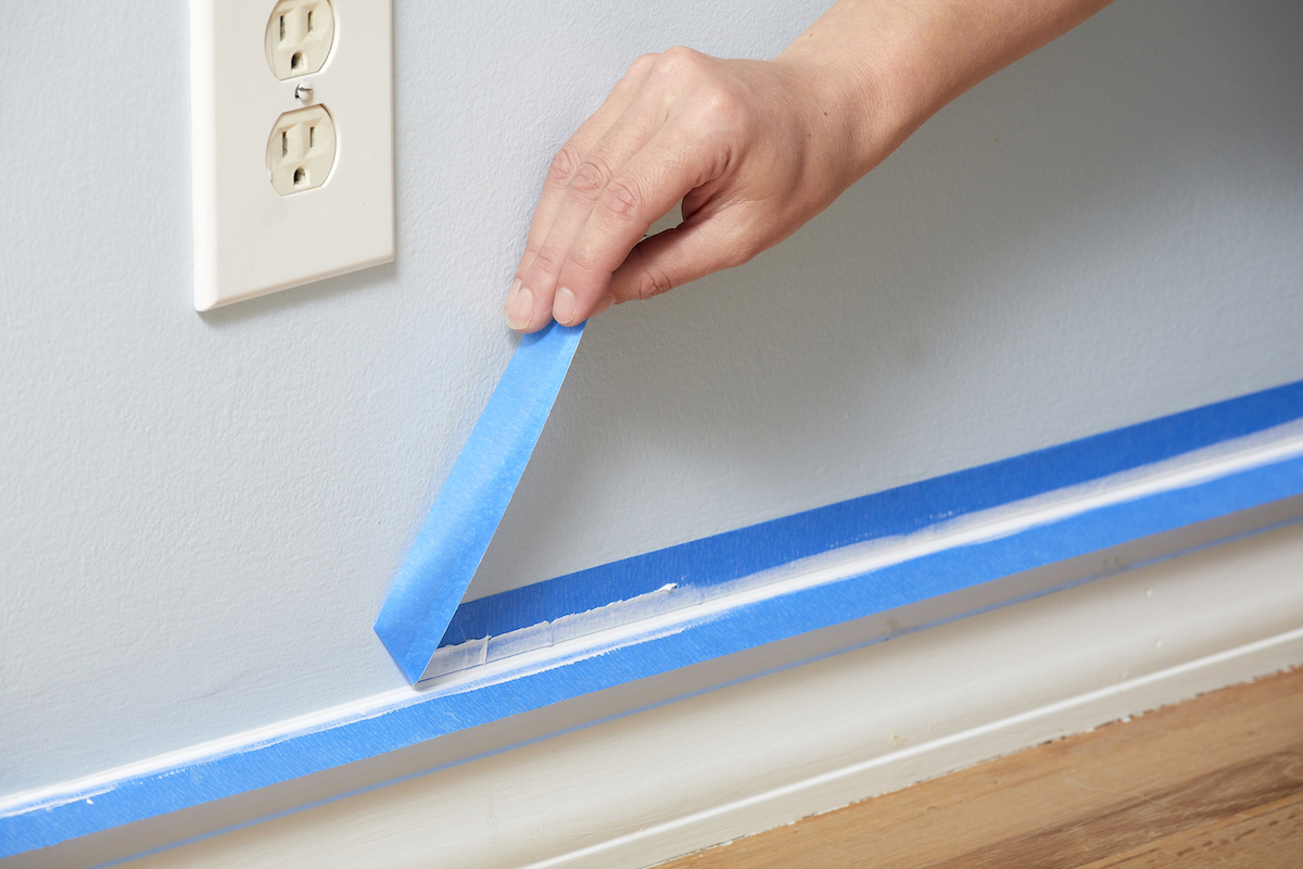 Woman removes painter's tape from above a baseboard.