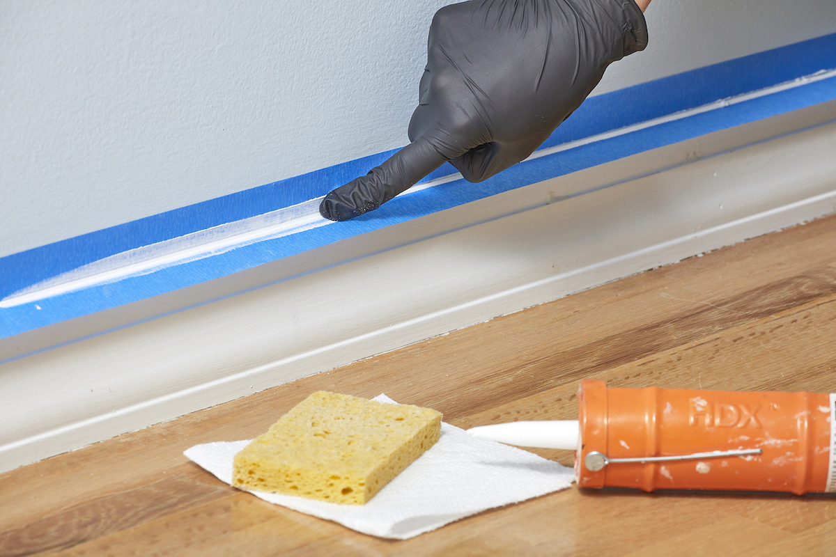 Woman wearing rubber glove smooths a caulk bead with her finger.