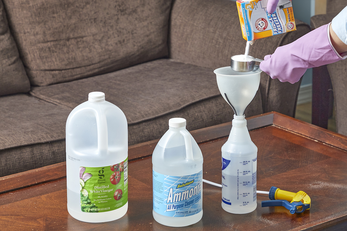 Woman pours baking soda through a funnel into a spray bottle, with bottles of vinegar and ammonia nearby.