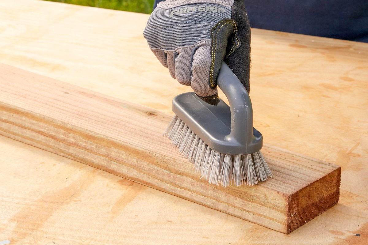 Woman uses scrub brush to clean a piece of pressure-treated wood.