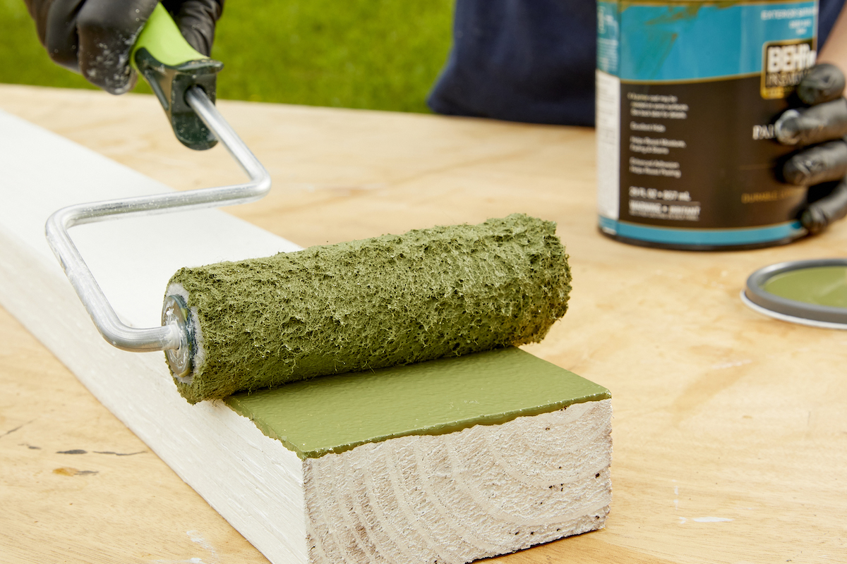 Woman paints one side of s a primed 2x4 with green paint.