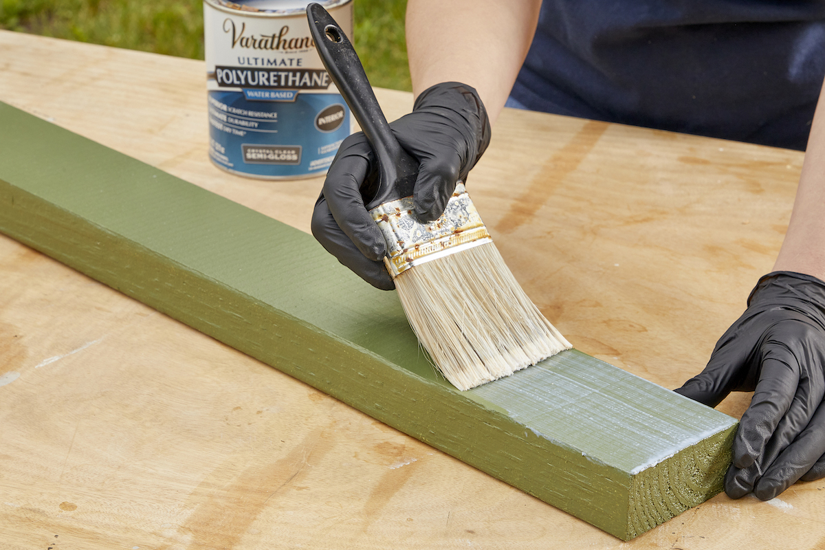 Woman paints a 2x4 piece of wood with polyurethane sealer.