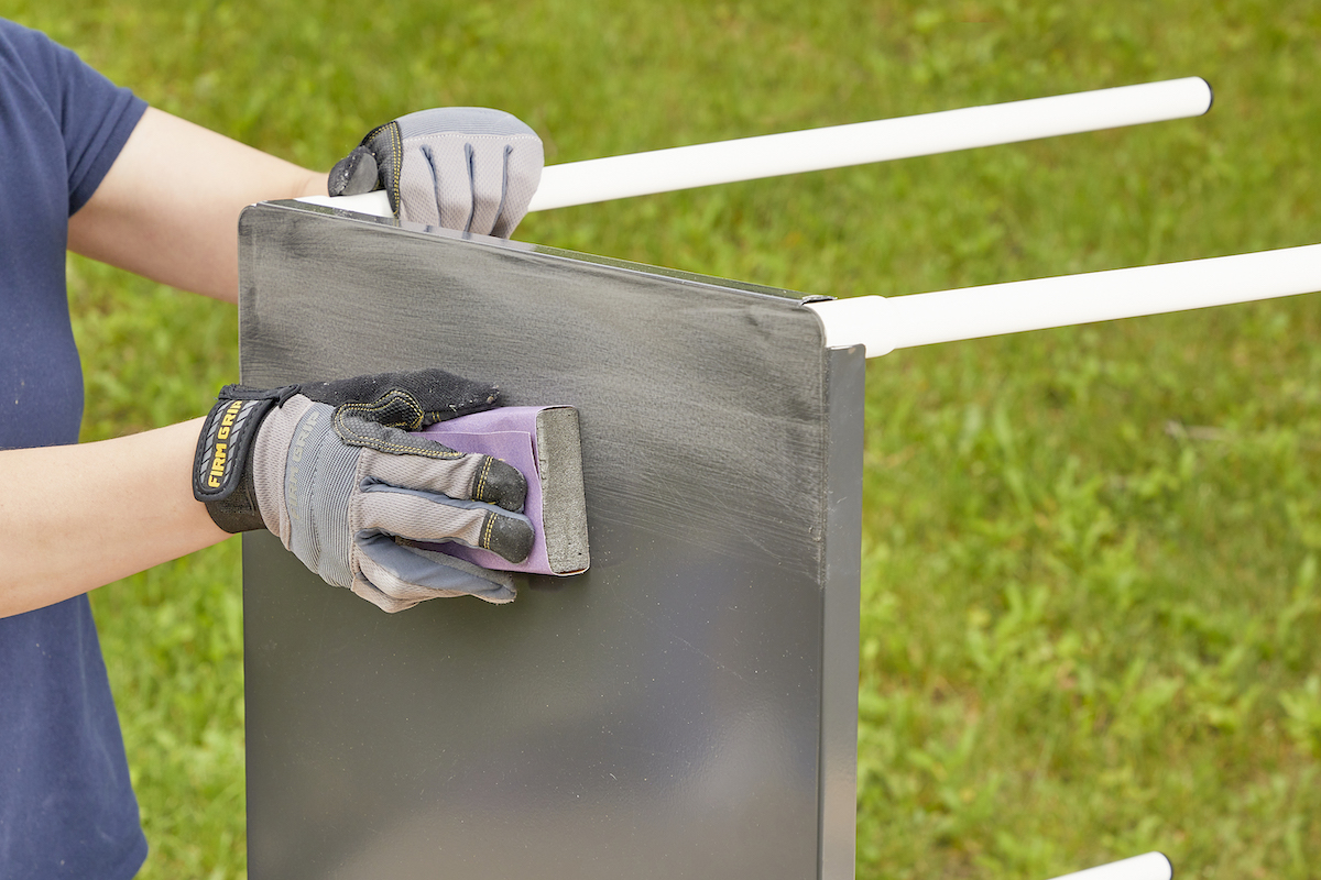 Woman uses sanding block to sand a metal table.