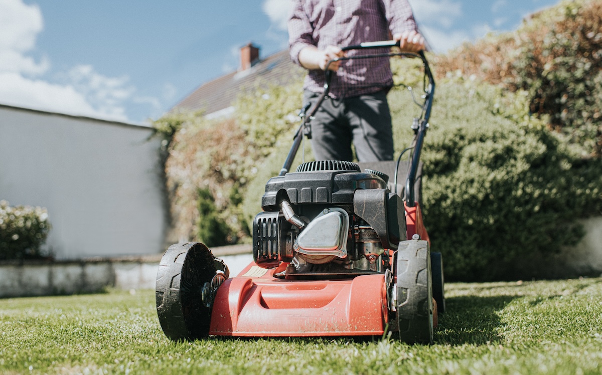 Man pushing a red lawn mower.