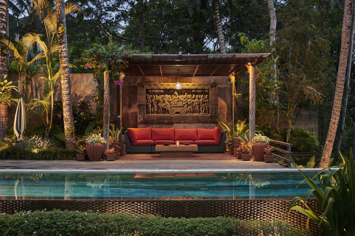 A poolside cabana in a home's backyard with a red patio couch and wooden architecture.