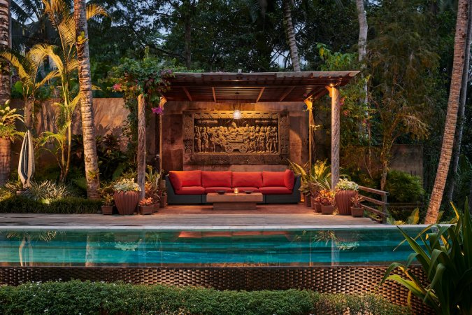 A poolside cabana in a home's backyard with a red patio couch and wooden architecture.