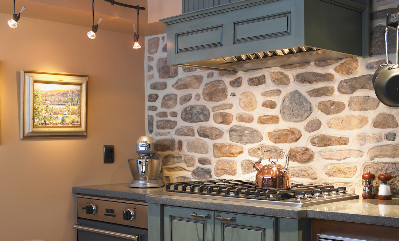 Gas kitchen cooktop with green hood and cabinets and a stone/masonry backsplash.