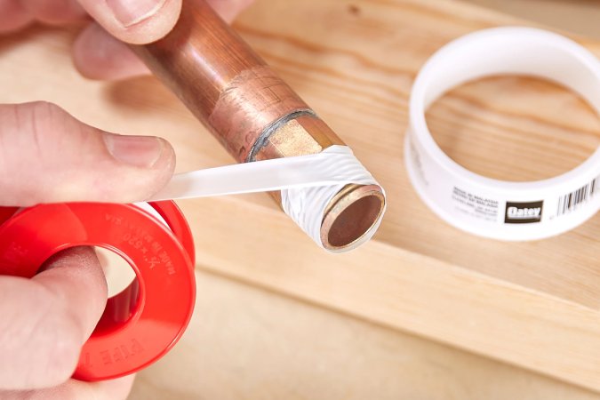 A person applies 1/2-inch Oatey plumber's tape to a male copper pipe's threading.