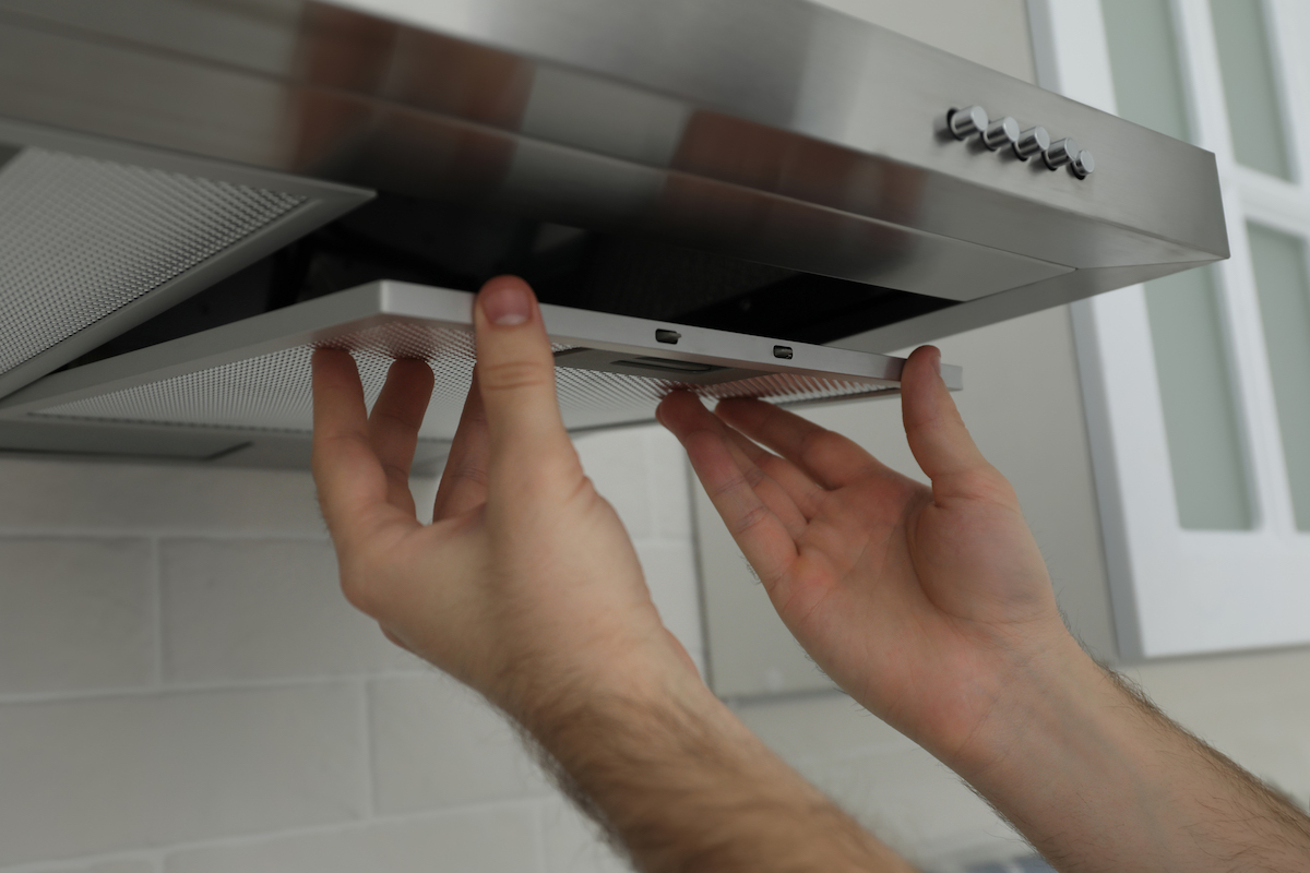 A person is using two hands to remove a range hood filter.