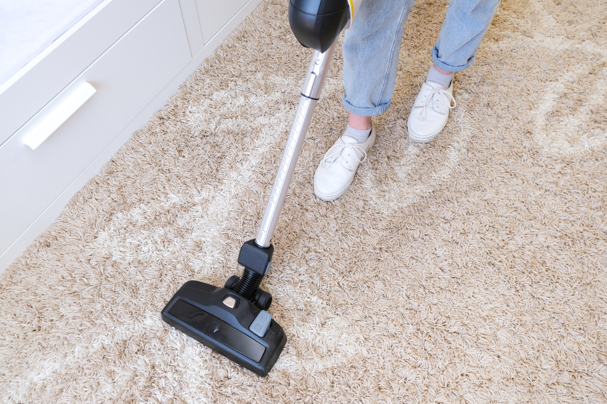 A woman with white shoes is vacuuming.